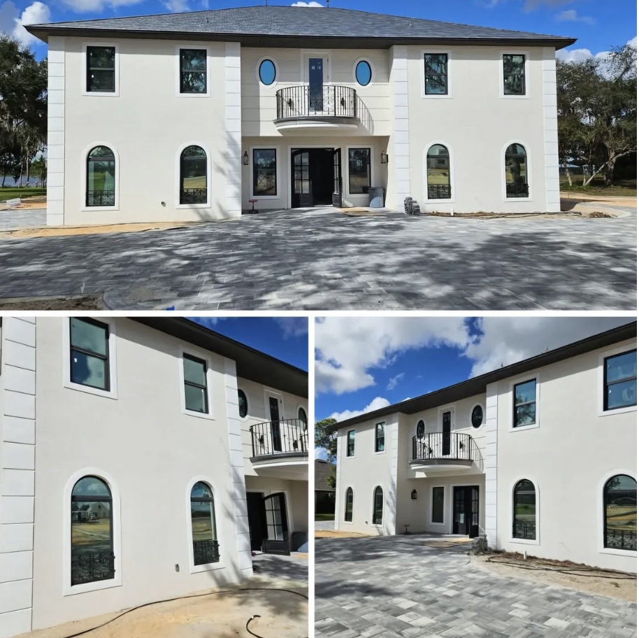 Modern two-story white house with black roof and dark windows, featuring a central balcony and paved driveway